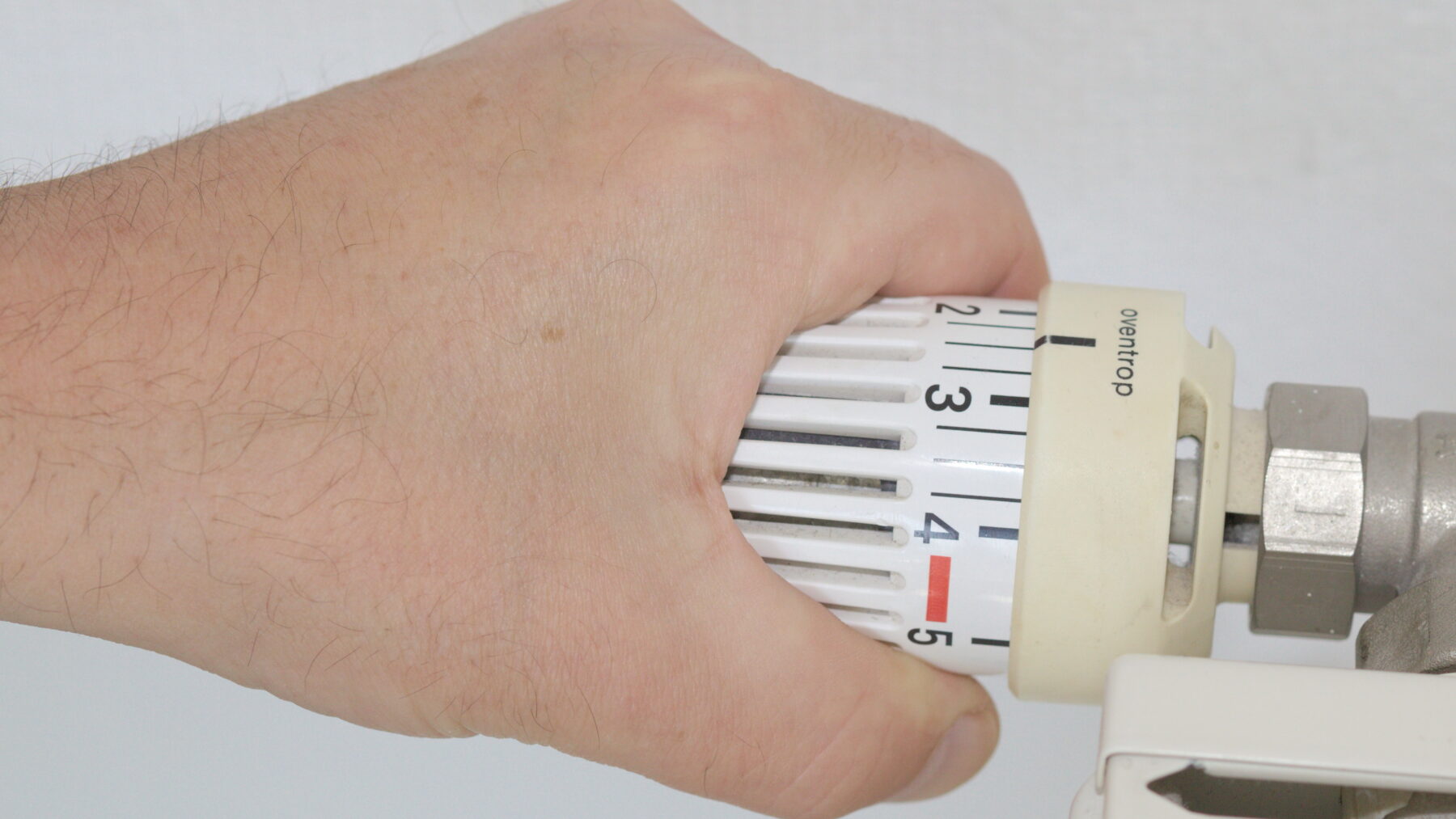 Una mano gira el cabezal graduado de una válvula termostática en un radiador de calefacción